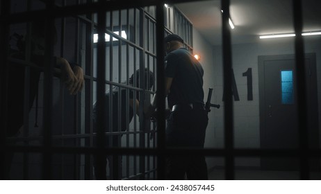 Warden brings new prisoner in jail cell and takes off his handcuffs. African American teen serves imprisonment term in correctional facility or detention center. Young inmates in jail. Tracking shot.