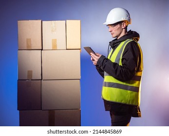 Warehouse And Box Manager. Fulfillment Center Employee. Man With Tablet Next To Boxes. Warehouse Manager In Studio Background. Man In Yellow Reflective Vest. Delivery Service Warehouse Worker