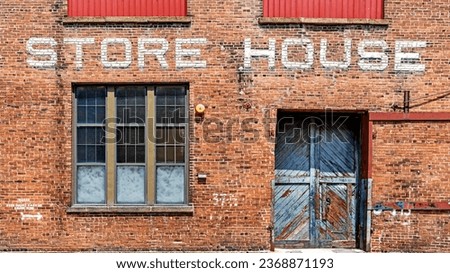 Warehouse brick front background with Store House stenciled above a beat up and damaged wooden blue double door and industrial style windows