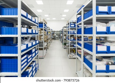 Warehouse of components for the electronics industry. White metal racks with blue plastic trays and cardboard boxes installed in them.
