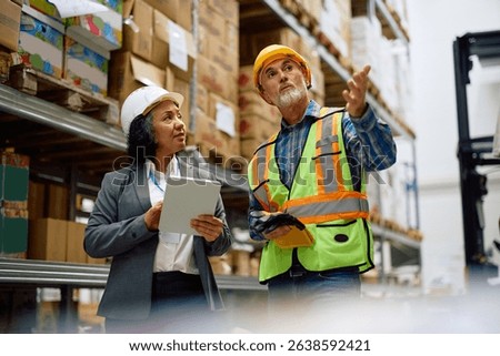 Warehouse inspector using touchpad while talking to a senior worker in storage room. 