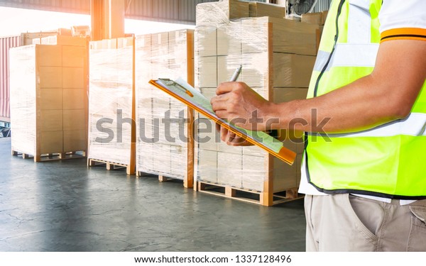 Warehouse inventory management. courier shipment\
transportation. Warehouse worker is writing on clipboard is\
checking the products in  distribution warehouse. stacked of\
cardboard boxes on\
pallet.