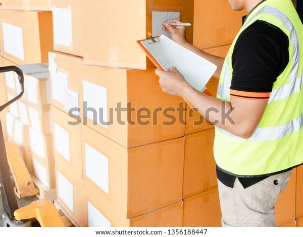Warehouse inventory and management, courier\
shipment transportation. Young warehouse worker is inspecting the\
products, stack of cardboard\
boxes.
