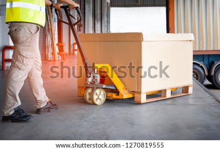 Warehouse loader dragging hand pallet truck or manual forklift with the shipment pallet at docks. 