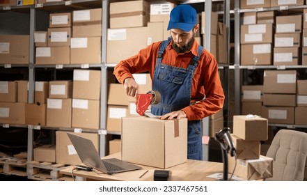 Warehouse male worker packing shipping ecommerce box checking website retail order preparing delivery parcel on table. Copy space - Powered by Shutterstock