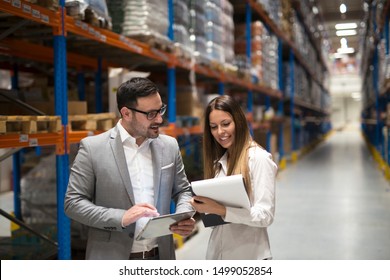 Warehouse management team checking organization and distribution in storage shipping center. Two beautiful elegant business people discussing about business improvement.