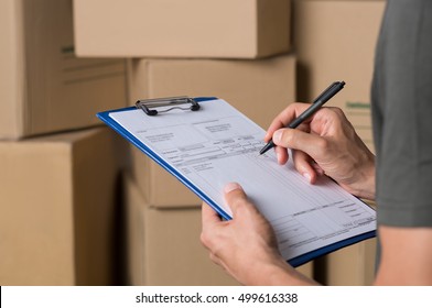 Warehouse manager signing dispatch sheet. Close up hand of manager checking delivery order. Young freight manager checking invoice with cardboard box parcel. - Powered by Shutterstock