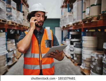 Warehouse Manager Tracking Supply Order Details Using Digital Tablet While In Conversation Over Mobile Phone In Warehouse