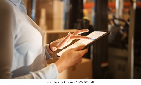 In Warehouse Manager Uses Digital Tablet with App to Check Package Delivery Status with Graphs, Infographics, and Statistics on Screen. Distribution Center with Shelves with Cardboard Boxes - Powered by Shutterstock