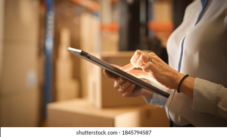 In Warehouse Manager Uses Digital Tablet Does Inventory, Using Touch Screen Gestures, Checking Package Delivery. Distribution Center with Shelves with Cardboard Boxes. Focus on Hands and Device