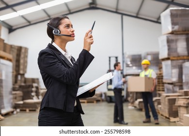 Warehouse manager wearing headset checking inventory in a large warehouse - Powered by Shutterstock