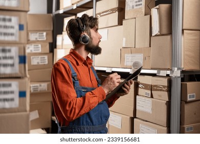 Warehouse manager wearing headset writing on clipboard working in a large warehouse checking checklist. Copy space - Powered by Shutterstock