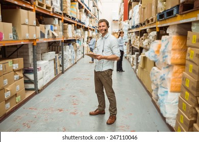 Warehouse manager wearing headset writing on clipboard in a large warehouse - Powered by Shutterstock