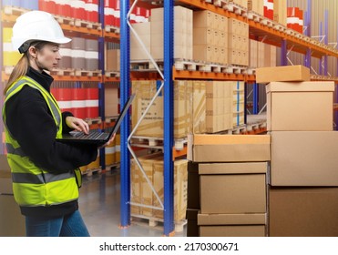 Warehouse Manager Woman. Girl In Protective Helmet In Front Parcels. Logistic Warehouse Manager With Laptop. Career In Logistics Industry. Girl In Yellow Vest Among Warehouse Racks. Logistics Manager