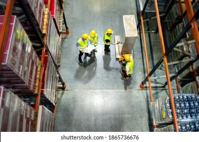 Warehouse Manager And Workers Consult Plans Between Tall Shelves, Above View