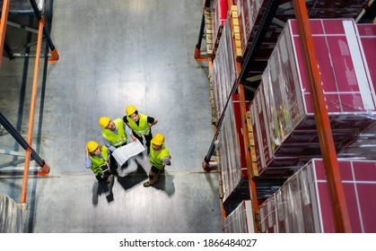 Warehouse Manager And Workers Consult Plans Between Tall Shelves, Above View