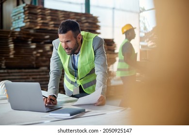 Warehouse manager working on laptop while going through paperwork at lumber distribution department. Copy space. - Powered by Shutterstock