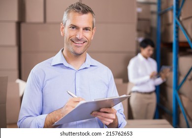 Warehouse manager writing on clipboard in a large warehouse - Powered by Shutterstock