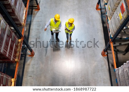 Warehouse managers consult plans using laptop, above view
