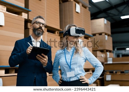 Warehouse managers talking logistics using VR, controlling stock levels. Virtual reality in inventory management. Smart glasses guiding female manager through warehouse, recording tracking data and