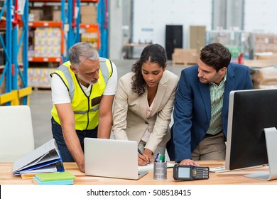 Warehouse Managers And Worker Discussing With Laptop In Warehouse Office