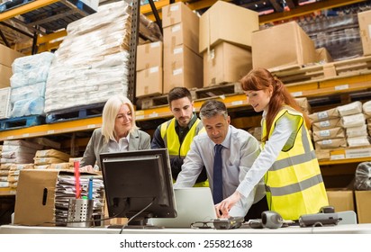 Warehouse managers and worker working on laptop in a large warehouse - Powered by Shutterstock