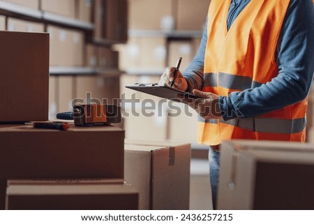 Warehouse operative checking a document on a clipboard and preparing a shipment