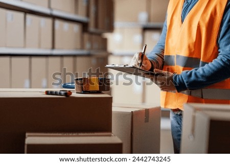 Warehouse operative checking a document on a clipboard and preparing a shipment