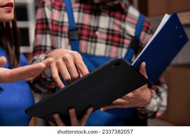Warehouse operators checking inventory data on digital tablet and analyzing orders checklist on clipboard. Storehouse postal managers colleagues comparing quality control reports