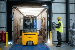 Warehouse Receiver Overseeing The Storing Of Delivered Items, Holding Tablet, Looking At Cargo Details. Forklift Carrying Pallets With Goods.