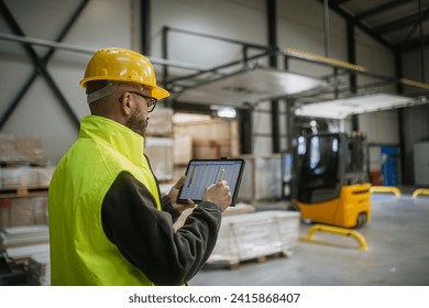 Warehouse receiver standing by delivered cargo, holding tablet, looking at cargo details, checking delivered items, goods against order. - Powered by Shutterstock