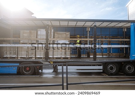 Warehouse receiver standing inside of truck in cargo area, trailer. Receiving clerk holding tablet, looking at cargo details, checking delivered items, goods against order.