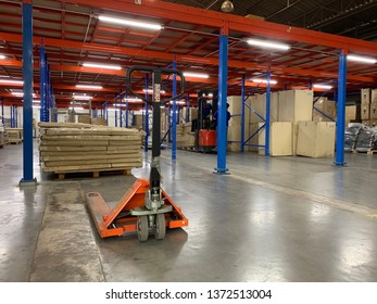 Warehouse Storage Of Retail Merchandise Shop, Worker Driver In Uniform Loading And Unload Cardboard Boxes By Forklift Stacker For Loader In A Large Modern Warehouse