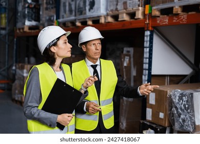 Warehouse supervisor instructing female employee in hard hat and safety vest, inspecting cargo - Powered by Shutterstock