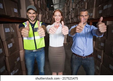 Warehouse team smiling at camera showing thumbs up in a large warehouse - Powered by Shutterstock