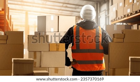 Warehouse worker with back to camera. Storekeeper stands among boxes. Man in orange vest. Guy works in warehouse building. Career in storage industry. Logistics warehouse worker. Fulfillment center