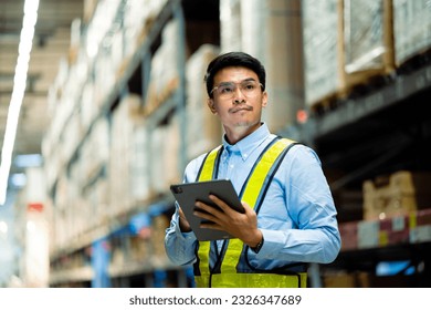 warehouse worker in a blue security suit uses a digital tablet to inspect inventory in a large warehouse. Distribution Center. Logistics and export of business. - Powered by Shutterstock