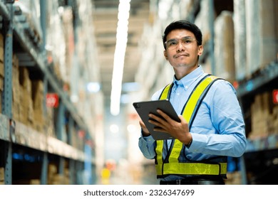 warehouse worker in a blue security suit uses a digital tablet to inspect inventory in a large warehouse. Distribution Center. Logistics and export of business. - Powered by Shutterstock