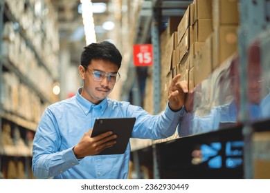 warehouse worker in a blue security suit uses a digital tablet to inspect inventory in a large warehouse. Distribution Center. Logistics and export of business. - Powered by Shutterstock