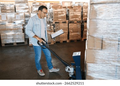 Warehouse worker checking cardboard boxes on a pallet with a manual pallet jack and clipboard in a spacious distribution warehouse, industry and business concept