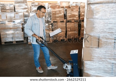Warehouse worker checking cardboard boxes on a pallet with a manual pallet jack and clipboard in a spacious distribution warehouse, industry and business concept