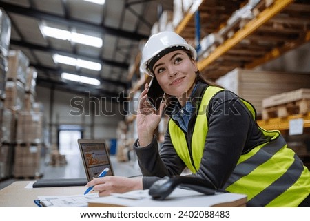 Warehouse worker checking delivery, stock in warehouse on computer, pc, while phone calling with contractor. Warehouse manager using warehouse management software, app.