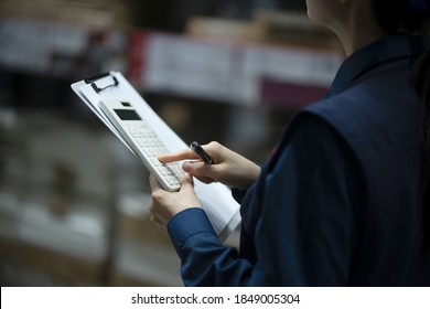 Warehouse worker checking inventory with calculator in logistics warehouse