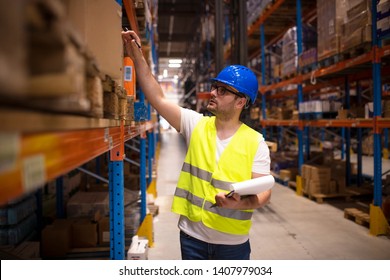 Warehouse worker checking inventory in large distribution warehouse. Industrial worker holding checklist in factory storage area.