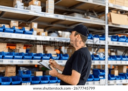 Warehouse worker checking inventory on shelves. A worker tallies items in a busy warehouse with organized shelves and blue storage bins.