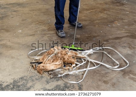 Warehouse worker cleaning up plastic packaging straps and fibreglass insulation from concrete floor. Concept of waste disposal, workplace safety, cleanliness, and industrial maintenance