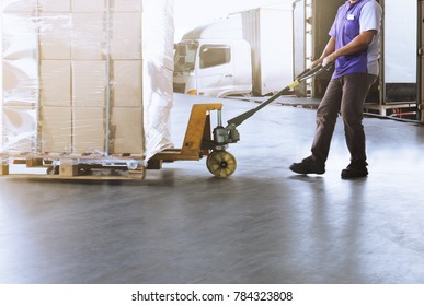 Warehouse worker dragging hand pallet truck or manual forklift with the shipment pallet unloading into a truck.
