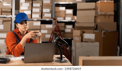 Warehouse worker drinking tea or coffee working in storeroom with rows of shelves of parcels, packages ready for shipment. Break on work. Copy space - Powered by Shutterstock