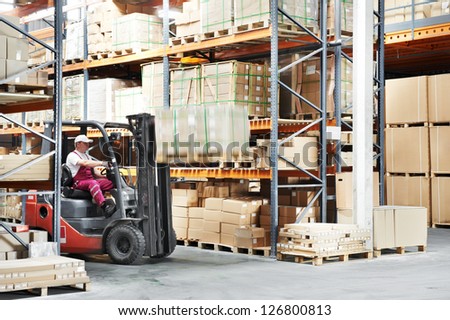 warehouse worker driver in uniform loading cardboxes by forklift stacker loader