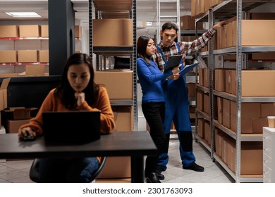 Warehouse worker and logistics manager doing products audit in storage room. Storehouse employees managing goods parcels quality control while analyzing data in clipboard and digital tablet